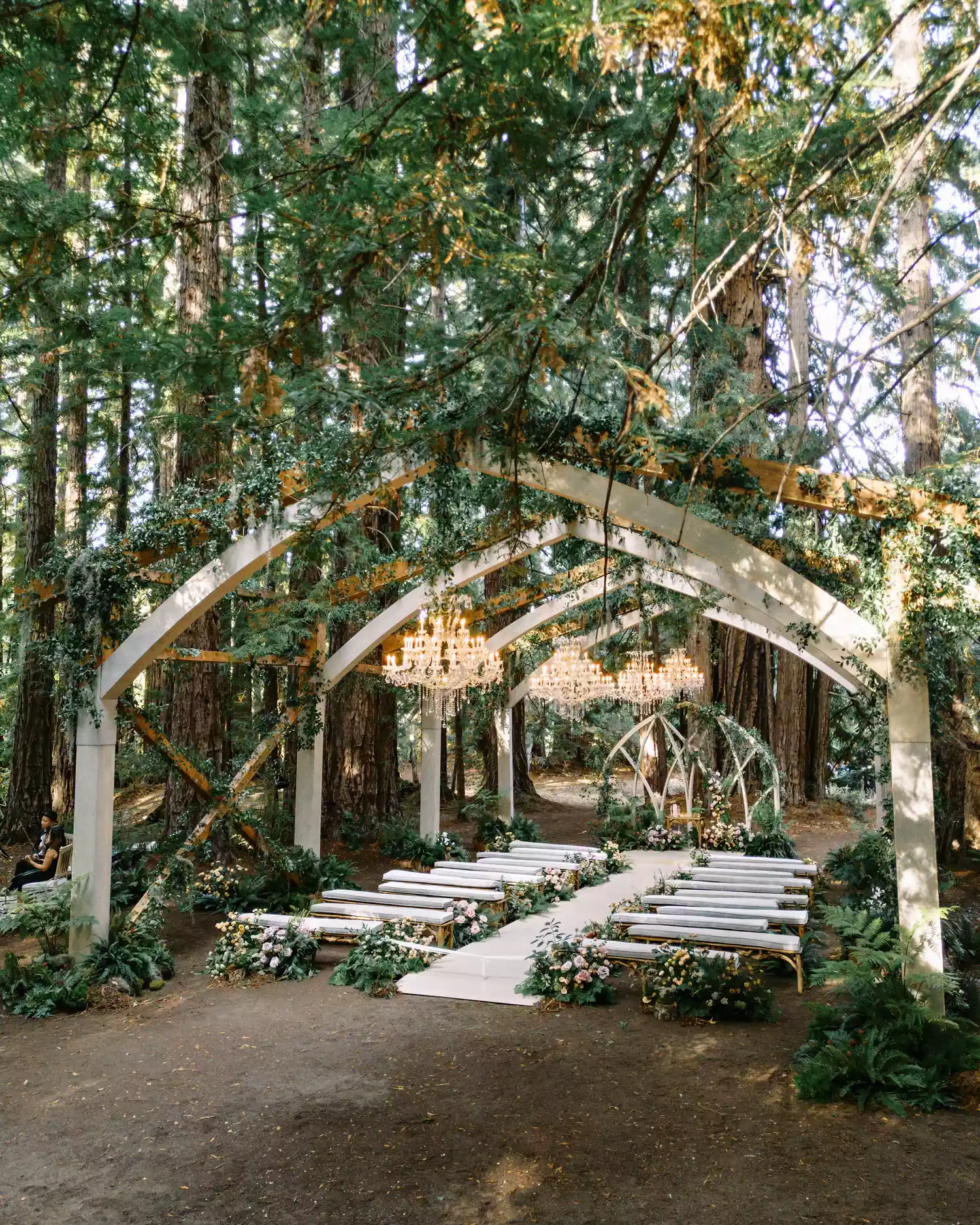 Outdoor Wedding Ceremony Under Wood Arch, Green Foliage, and Chandeliers