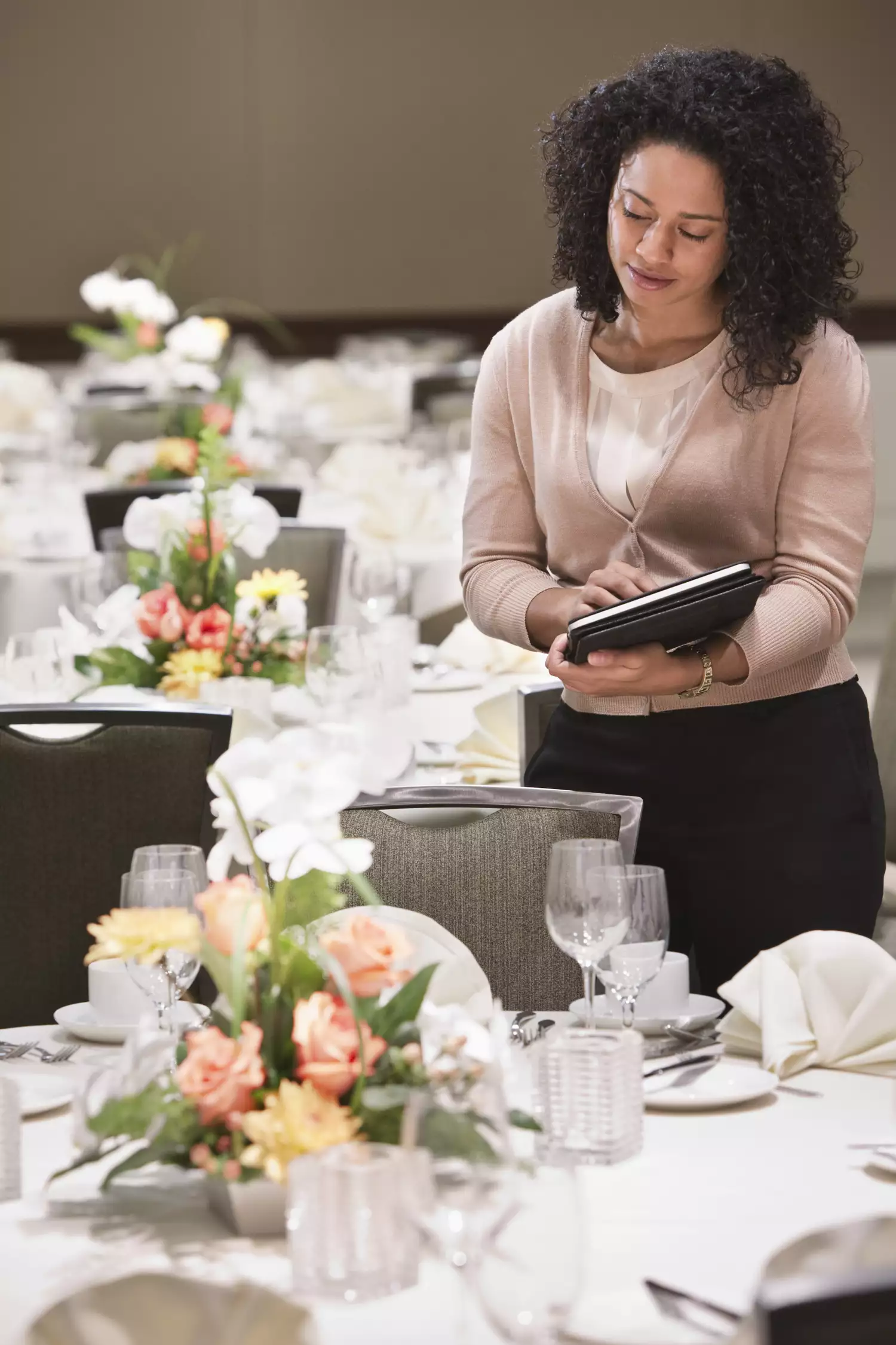 Black Woman Holding iPad and Looking at Reception Table With Floral Centerpiece