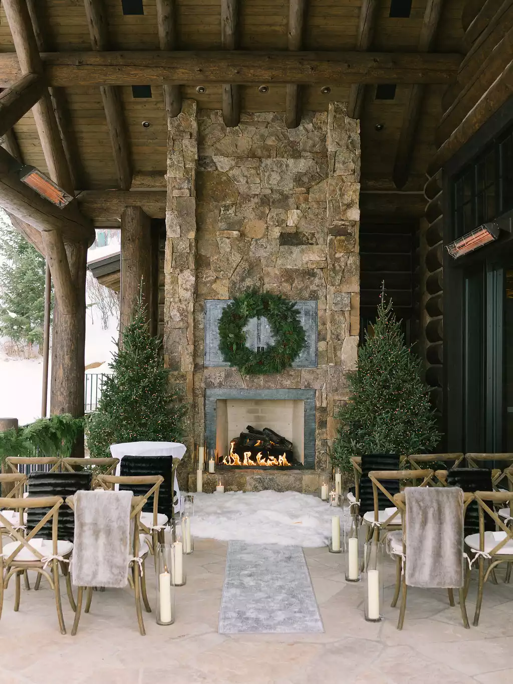 A ceremony setup with a stone fireplace, a greenery wreath, and two Christmas trees for the altar