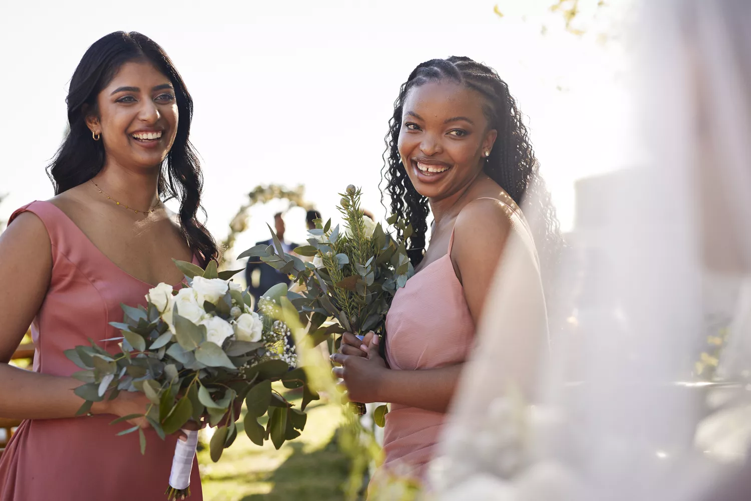 two bridesmaids in dusty rose dresses holding green bouquets during outdoor wedding ceremony