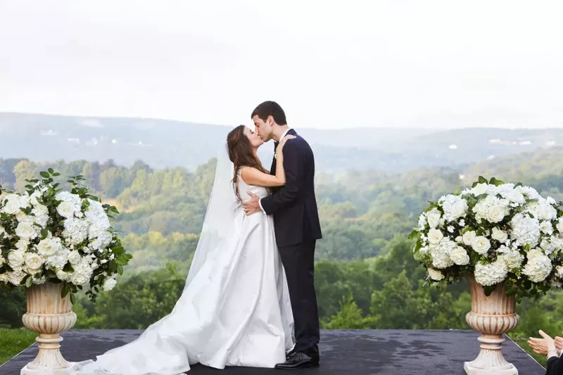 Couple kissing during backyard wedding overlooking mountains and surrounded by white flowers.