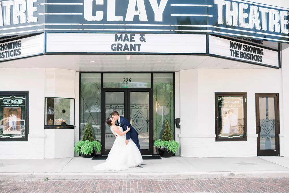 Bride and groom kissing in front of a theater marquee at Clay Theater during a wedding ceremony.