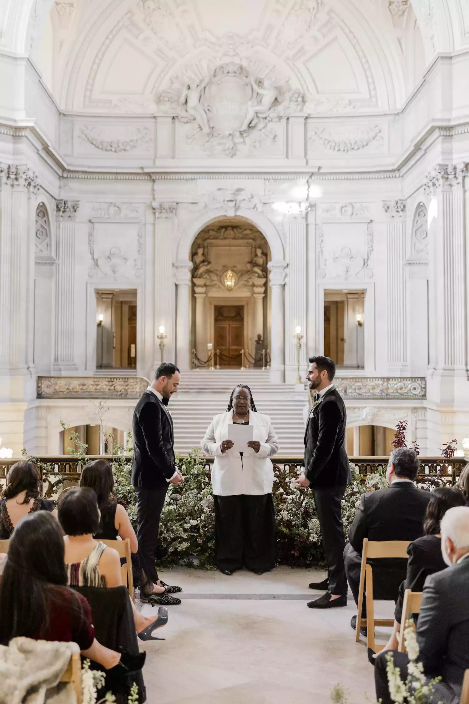 two grooms in black tuxedos standing at the altar overlooking San Francisco City Hall