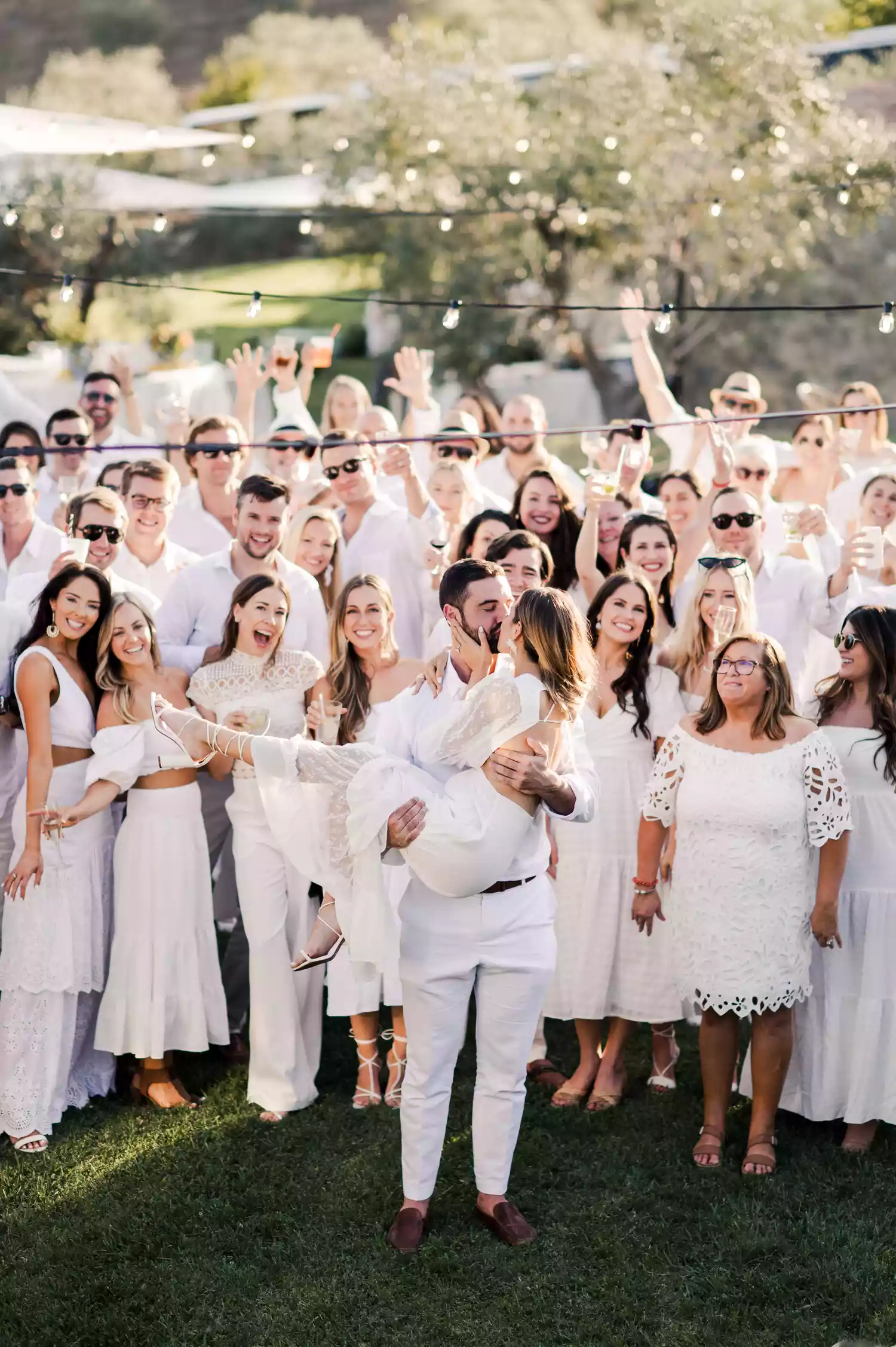 Bride and groom kissing in front of their guests all dressed in white attire