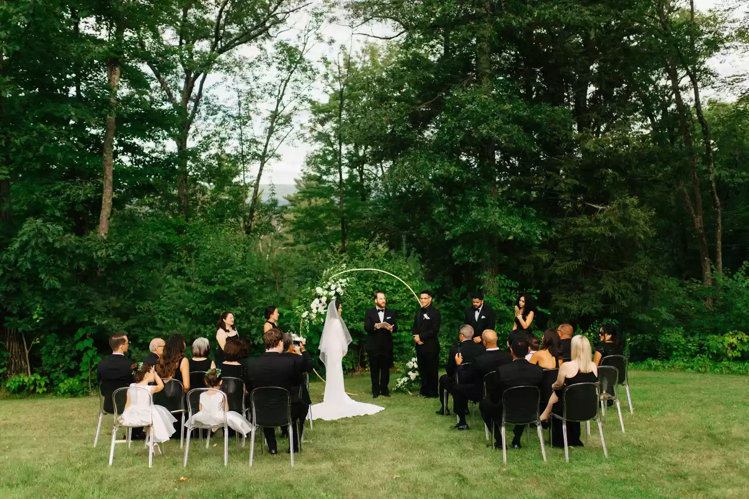 bride and groom standing in front of gold arbor facing their 20 guests