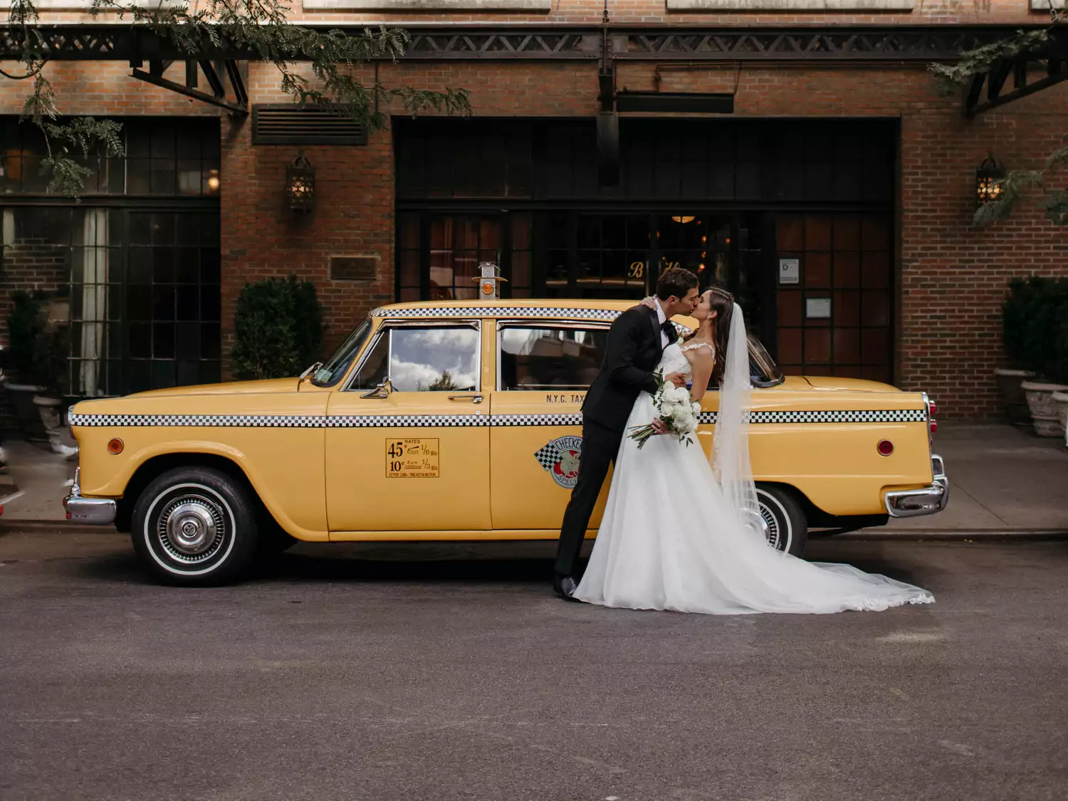 bride and groom kissing in front of a yellow taxi