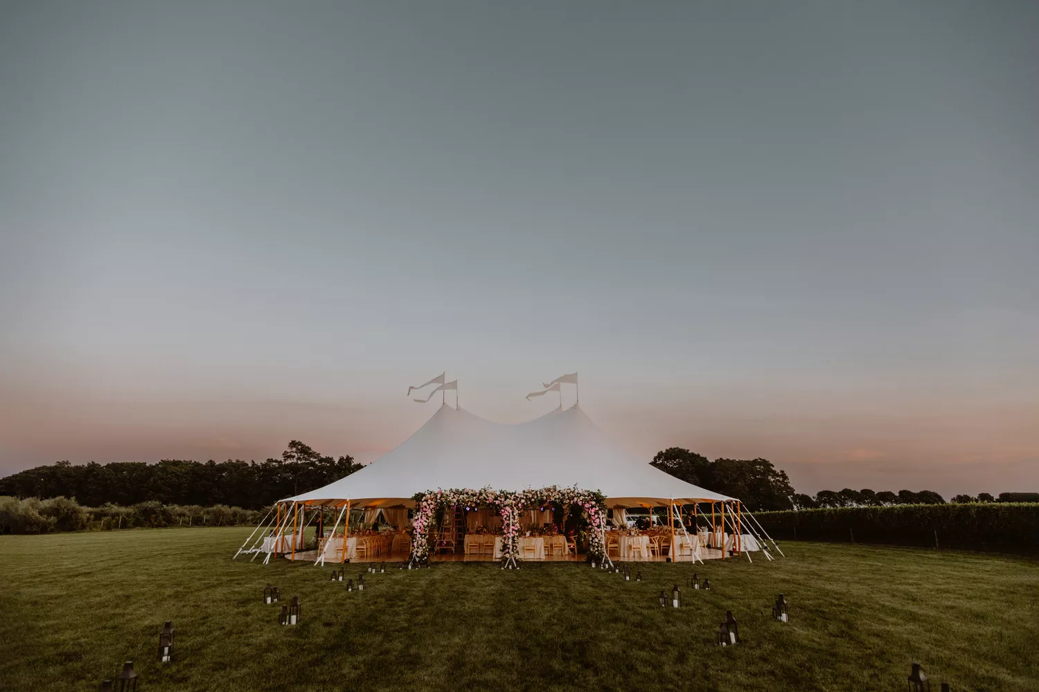 White wedding tent with fresh pink floral arch at an outdoor wedding venue at sunset in the summertime.