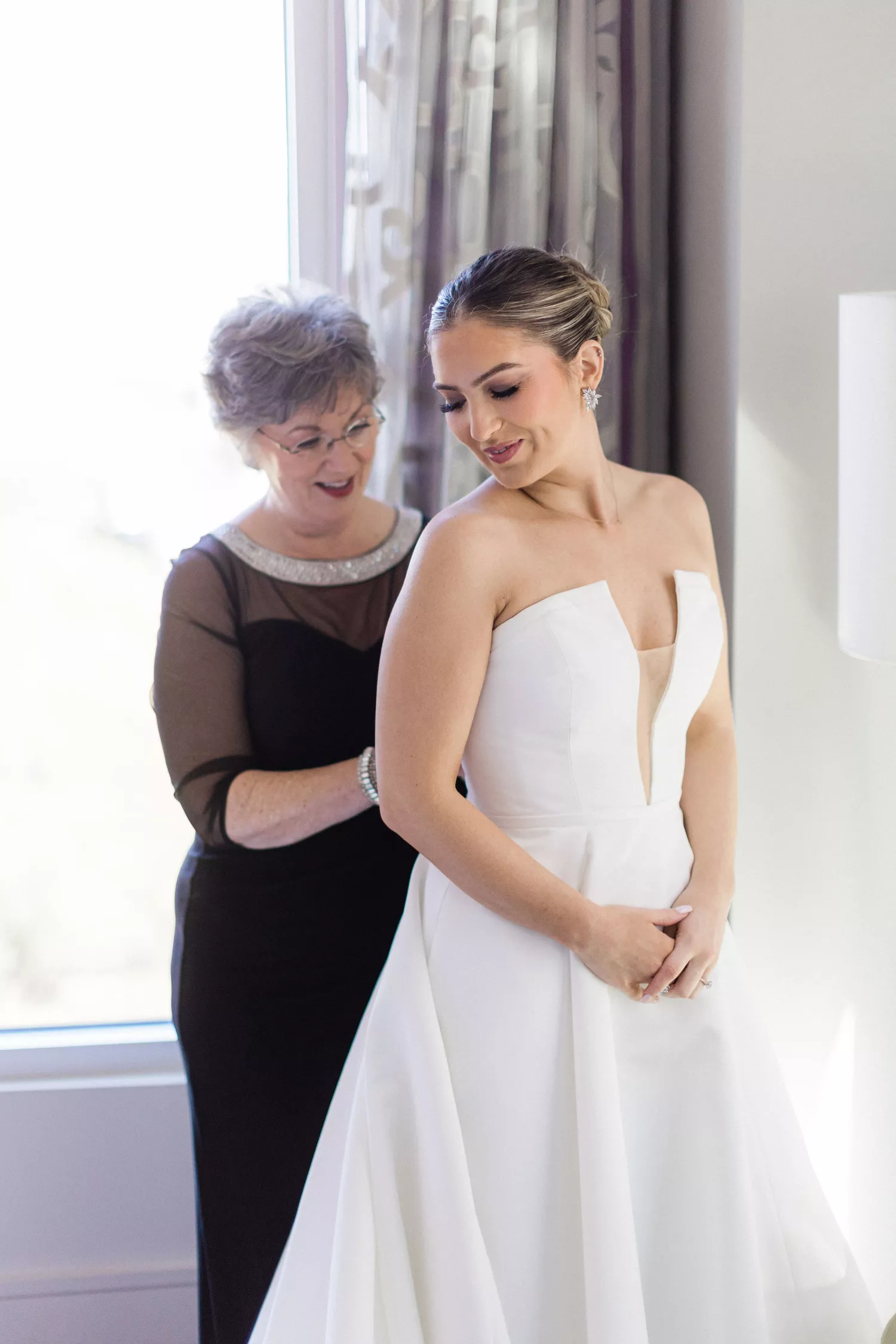 mother of the bride helping her daughter, the bride, put on her wedding dress