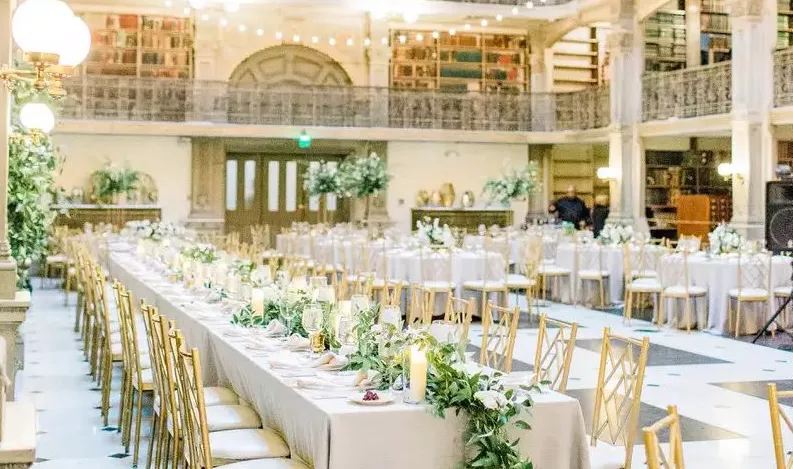 Long white reception tables with candles and flowers, string lights above at Peabody library