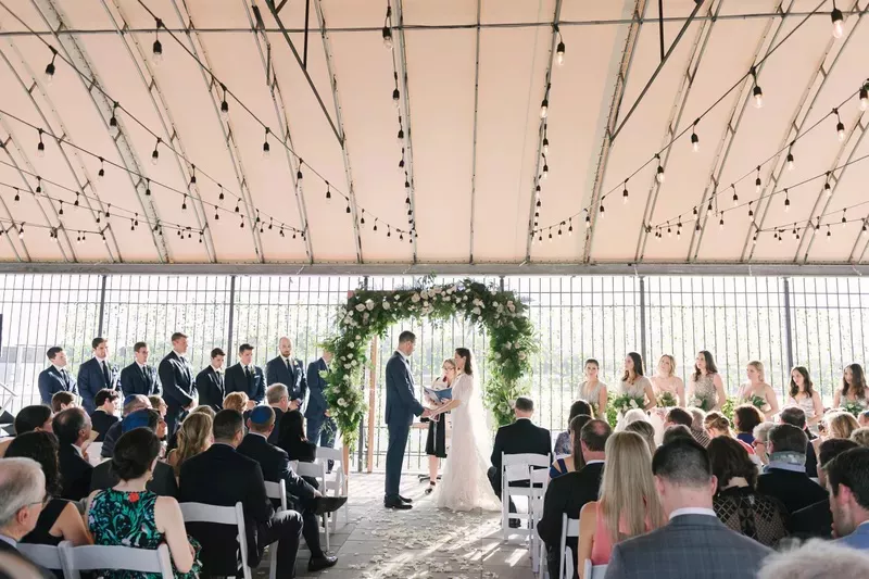 Wedding ceremony under a tent with a flower-covered arch at City Winery.