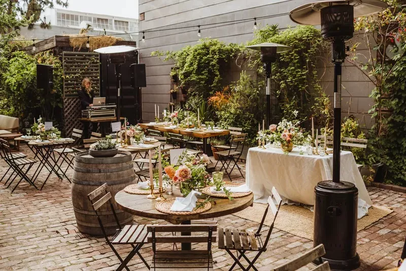 Stable cafe wedding reception outside with small wooden tables set with floral arrangements and candles.