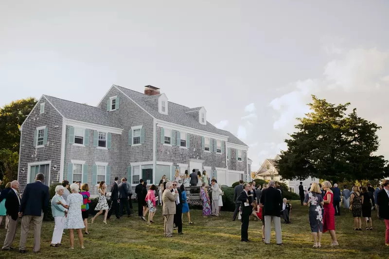 A backyard wedding with guests outside of a grey shingled New England home.