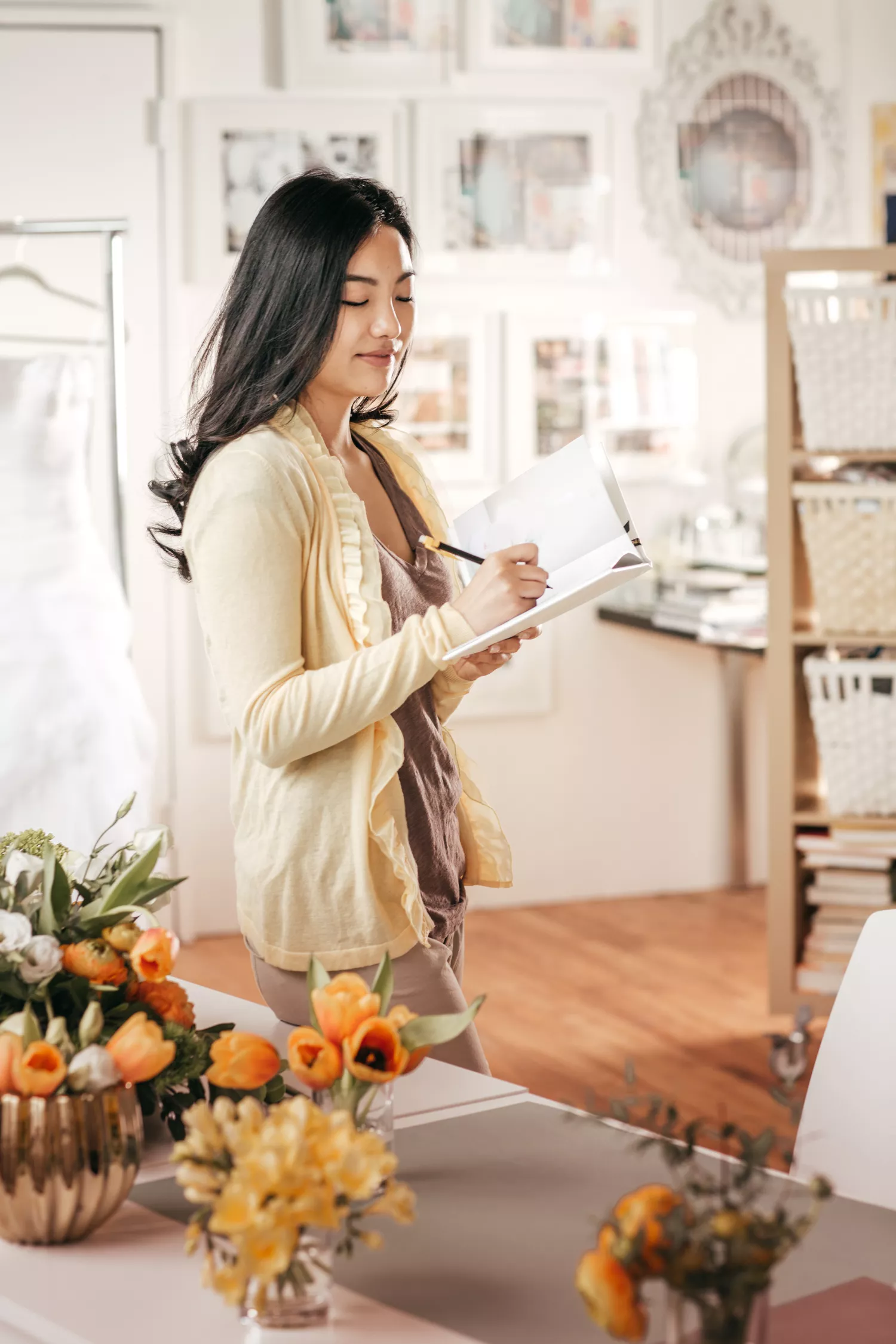 Dark-Haired Woman Writing in Notebook Next to Orange Floral Arrangements