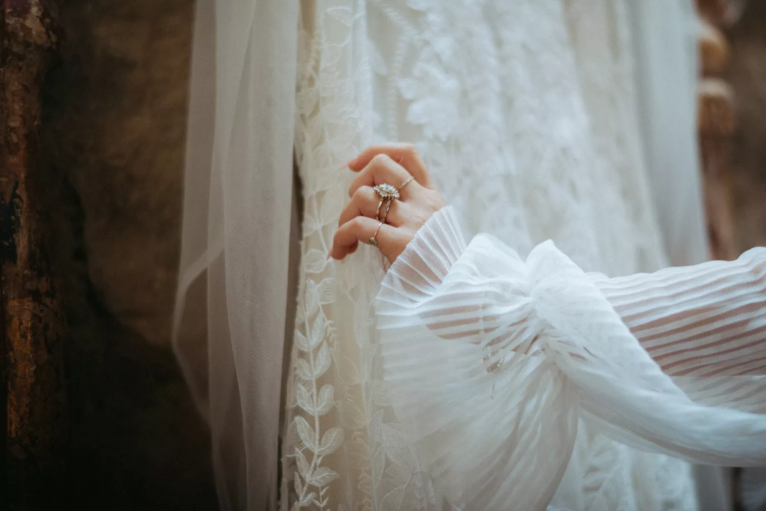 a photo of a bride's hand with multiple ring holding a lace dress