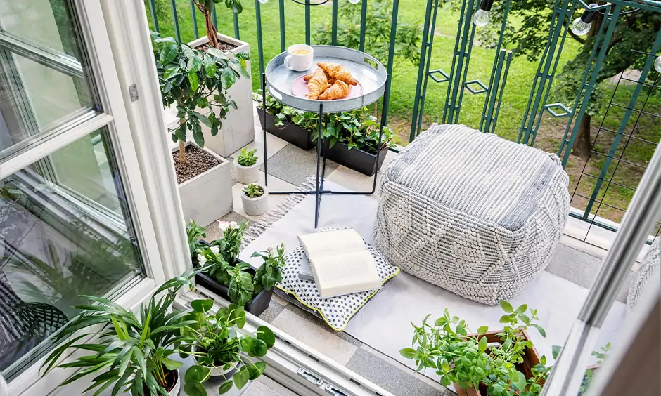 White and green-themed DIY balcony seating with a pouffe, rug, small cushion and natural potted plants looks classy.